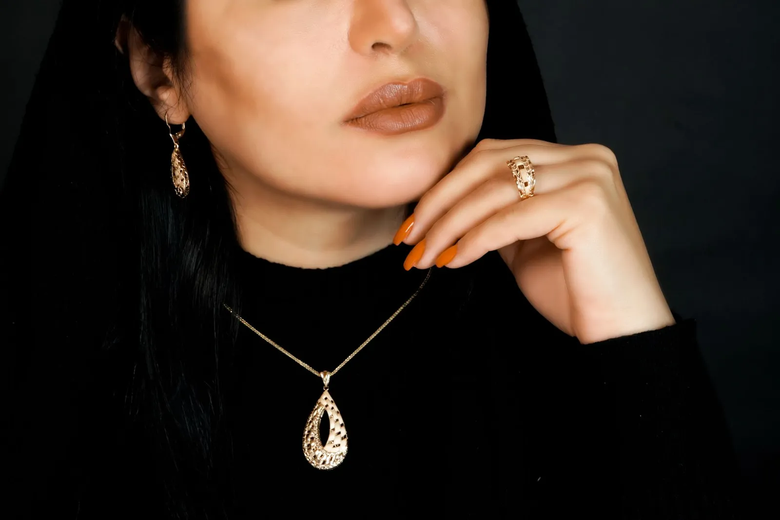 Woman in a black jumper wearing a golden teardrop pendant, earrings and a gold ring