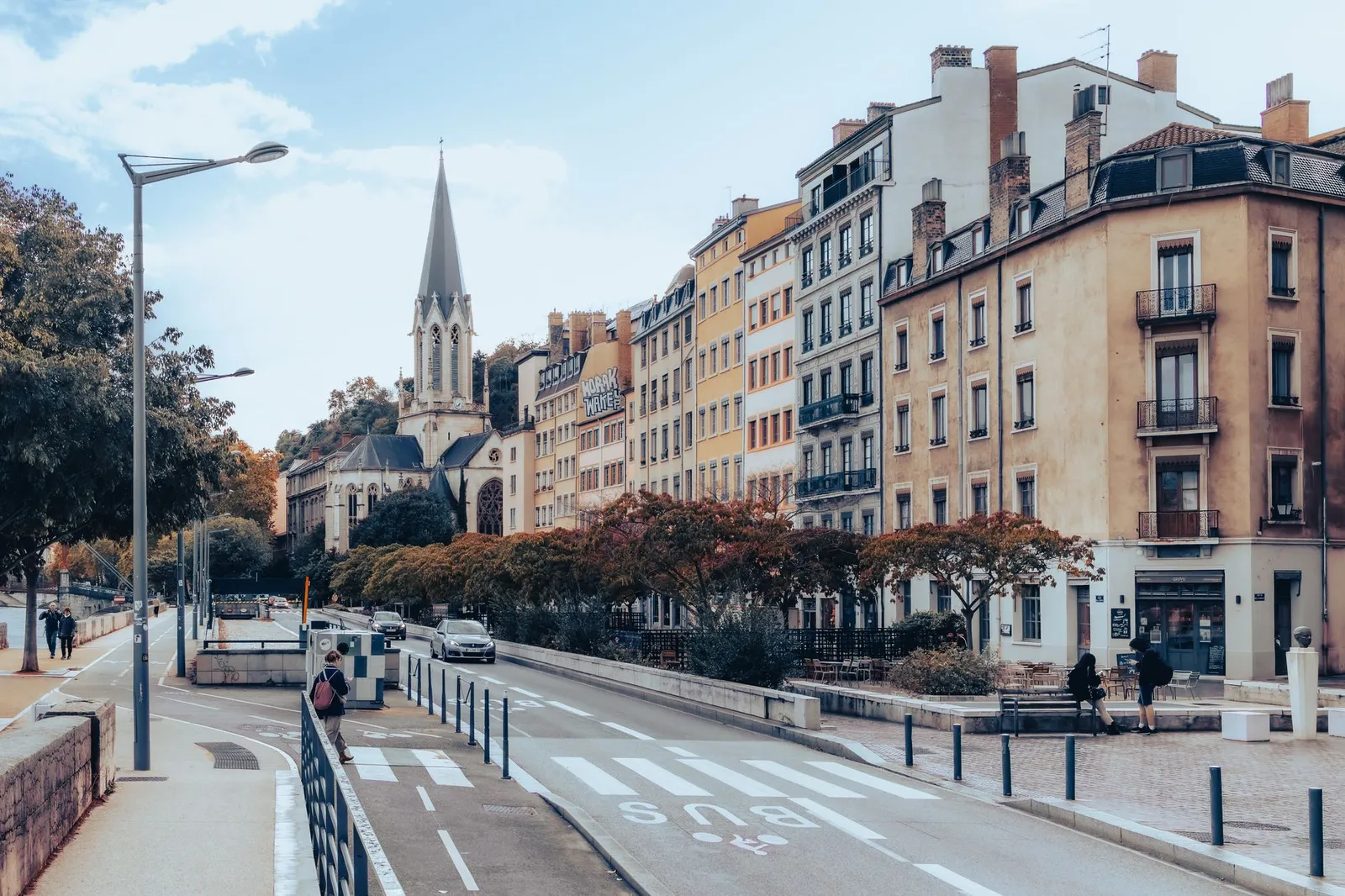 Lyon street lined with pale historic buildings, a church spire at the end of the avenue