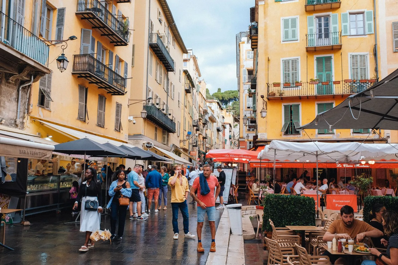 Pedestrian street in Nice lined with yellow facades, terraces and parasols, passers-by in the late afternoon