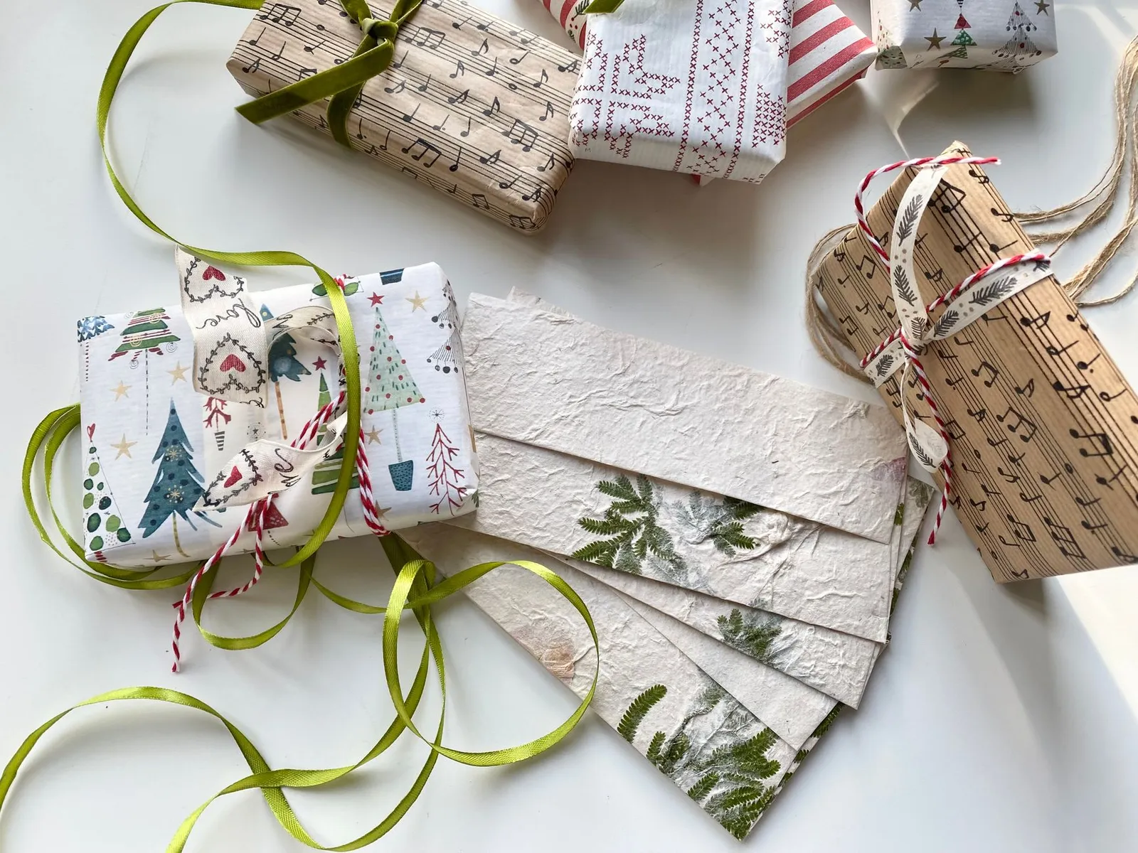 Gifts wrapped in printed papers, green ribbons and a small woven basket on a white table