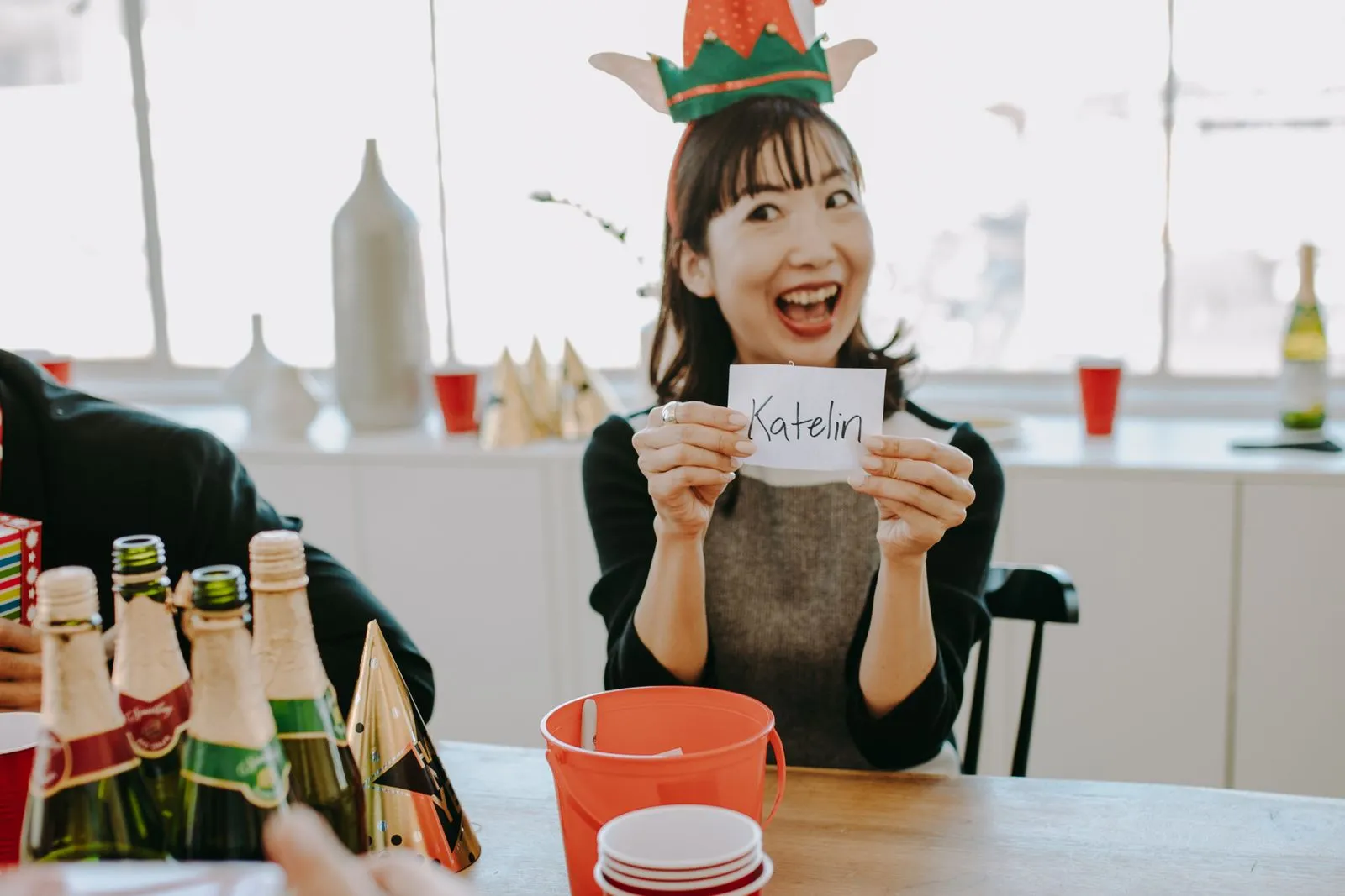 Une participante montre, amusée, le prénom tiré au sort pour un Secret Santa, autour d'une table de fête