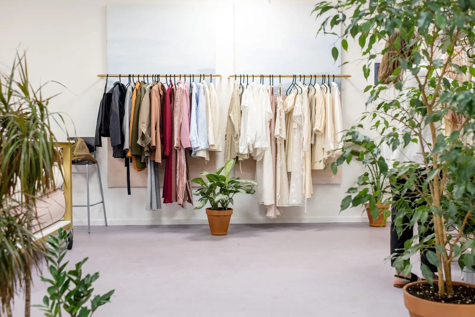Rail of light-coloured clothes in a bright boutique surrounded by green plants