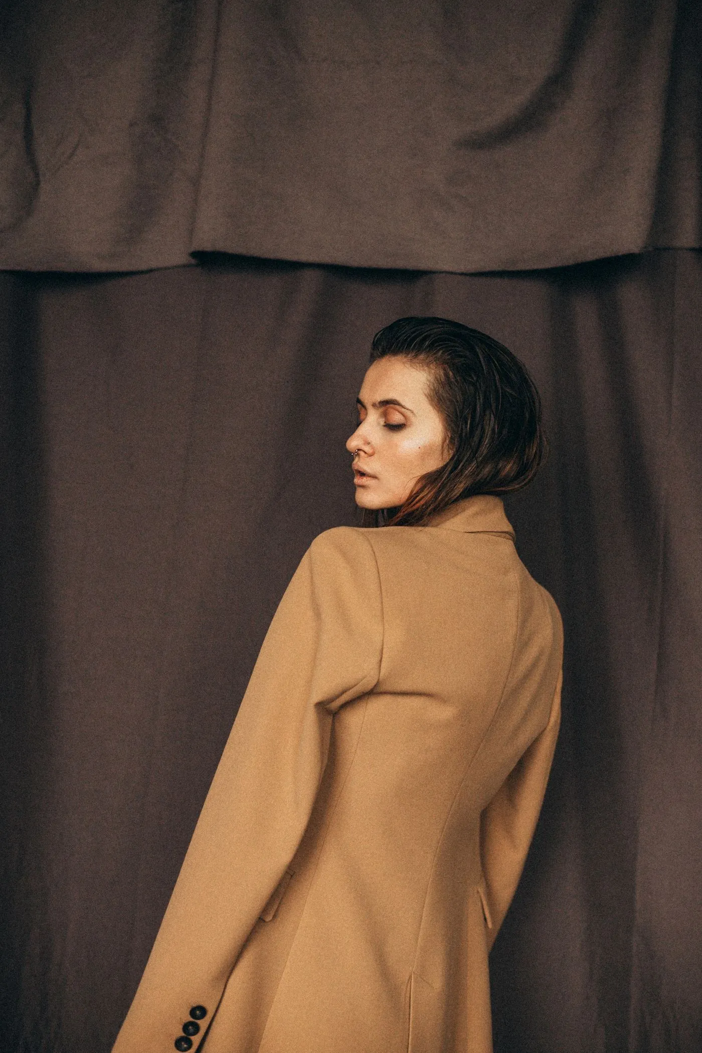 Femme en blazer camel devant un drapé sombre